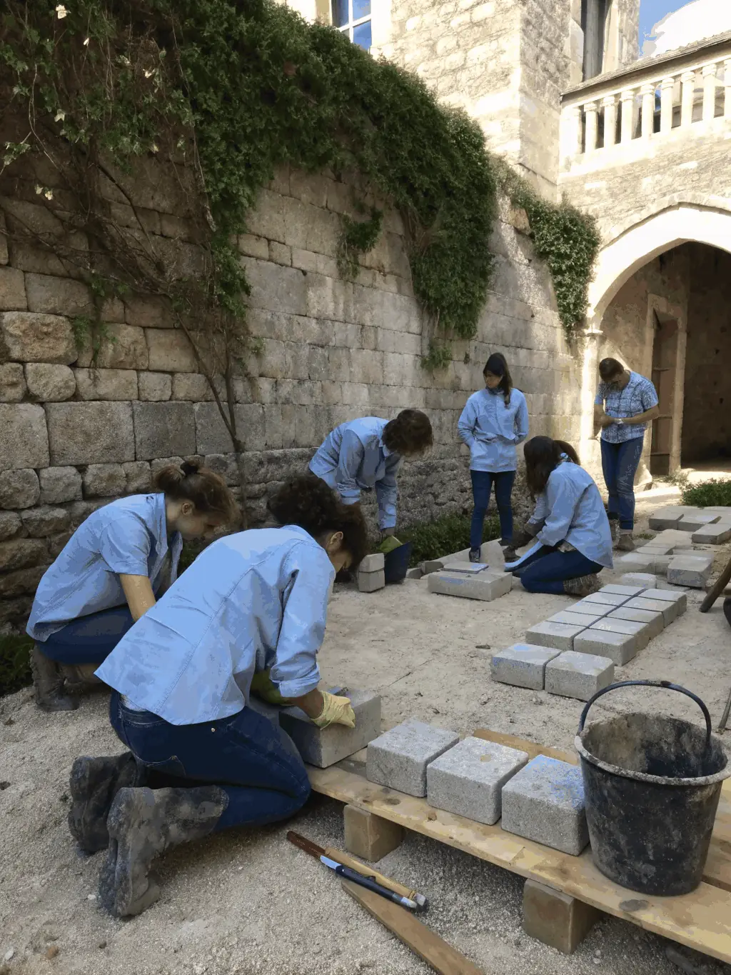 A group of children and adults participating in a hands-on heritage workshop, learning traditional masonry techniques in the château’s courtyard.